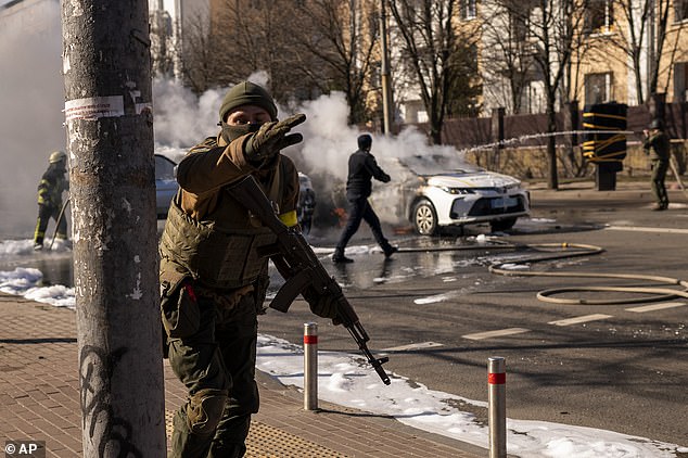 Ukrainian soldiers occupy positions in front of a military facility while two cars burn on a street in Kiev, Ukraine on Saturday.  Russian troops stormed the Ukrainian capital on Saturday and sparked street fighting