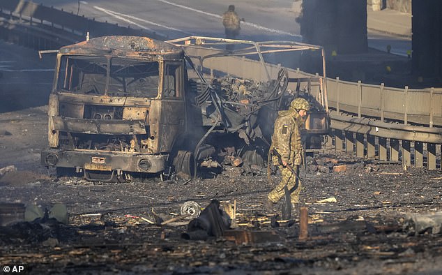 Ukrainian soldier passes by wreckage of burning military truck on street in Kiev, Ukraine, Saturday