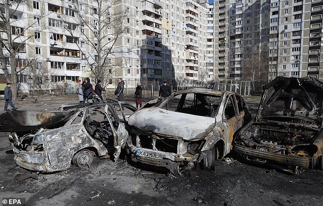 People pass burnt cars the day after a shelling of a residential area in the Ukrainian capital Kyiv.  The country is on its fifth day of fighting since Russia's invasion on Thursday