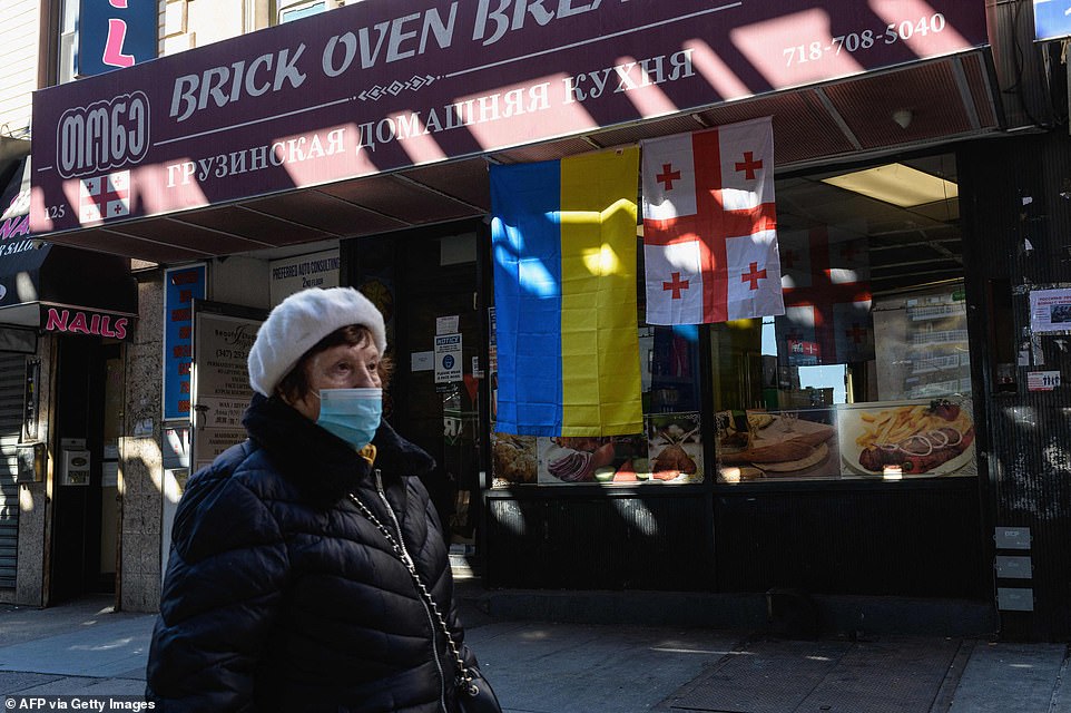 A woman walks past Ukrainian and Georgian flags in front of a Brighton Beach store, also known as "Little Odessa" thanks to the close-knit Russian and Eastern European communities