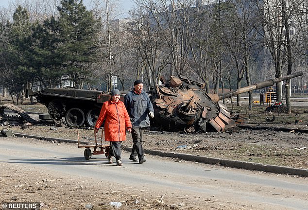 People walk past a tank destroyed in the fighting during the Ukrainian-Russian conflict, in the besieged southern port of Mariupol, Ukraine, March 23, 2022.