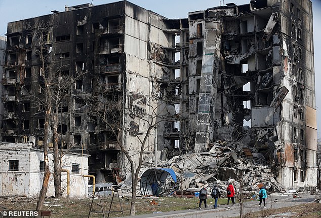 Local residents walk near an apartment building destroyed during the Ukraine-Russia conflict in the besieged southern port city of Mariupol, Ukraine, March 30, 2022