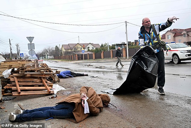 The body of a civilian with his hands tied behind his back lies on the street while a municipal worker prepares a plastic body bag to carry it