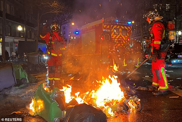 French firefighters extinguish burning bins after a demonstration in Paris on Monday night, the day the National Assembly debated and voted on two motions of no confidence in the French government