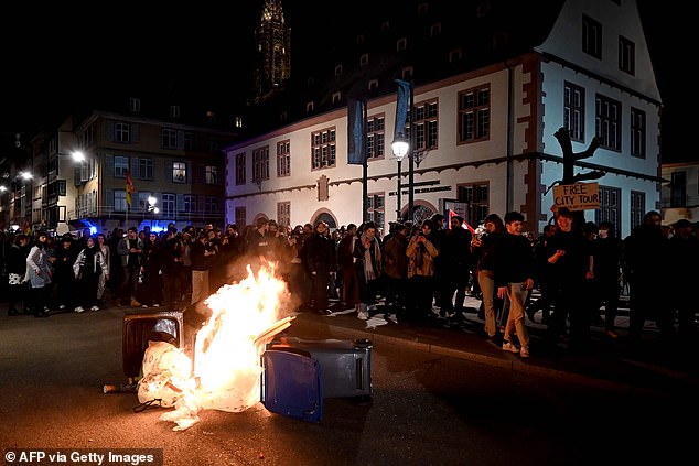 Protesters march next to a fire during a demonstration Monday night after the French government survived two no-confidence motions in parliament