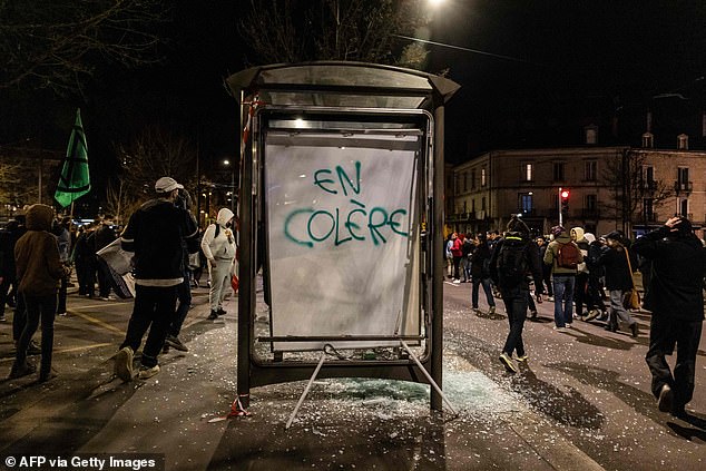 Protesters walk past a damaged bus stop during a demonstration in Dijon, central France, Monday night, who they describe as 