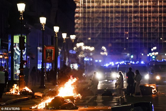 People walk past burning rubbish bins near the Opéra Garnier in Paris on Monday evening