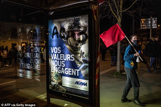 A protester with a red flag walks past a bus stop that has a poster for a pension group on it that reads "Our values ​​oblige us"during a demonstration in Dijon on Monday