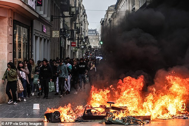 Pedestrians walk past a fire made of household rubbish during demonstrations in Bordeaux, southwest France, on Saturday