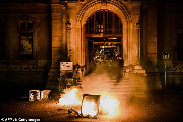 A French police officer tries to extinguish flames at the entrance of a city hall in Lyon after a protest on Friday evening