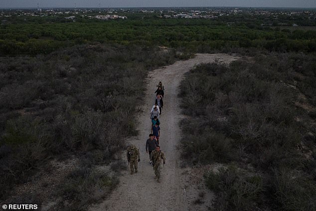 Mexico is seen in the background as soldiers from the Texas Army National Guard lead migrants after they were smuggled across the Rio Grande River into Roma, Texas on Thursday