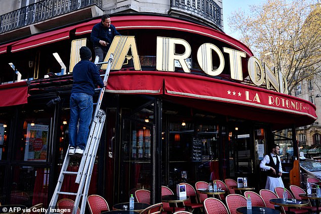 Workers repair the sign of La Rotonde restaurant in Paris that partially burned down during protests