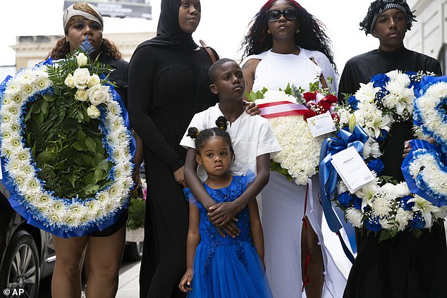 Heartbroken family members hold blue and white floral riffs during Tuesday's celebration of life as they mourn the loss of their loved one