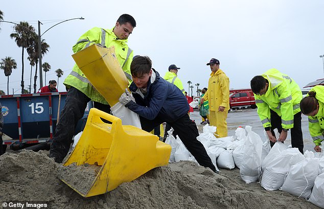 Volunteers and members of the Long Beach Fire Department fill sandbags in front of Hilary at Belmont Shore Beach