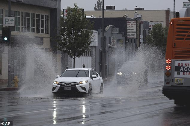 A vehicle splashes through puddles along a street beginning to flood in the Van Nuys neighborhood of Los Angeles as a tropical storm sweeps the area