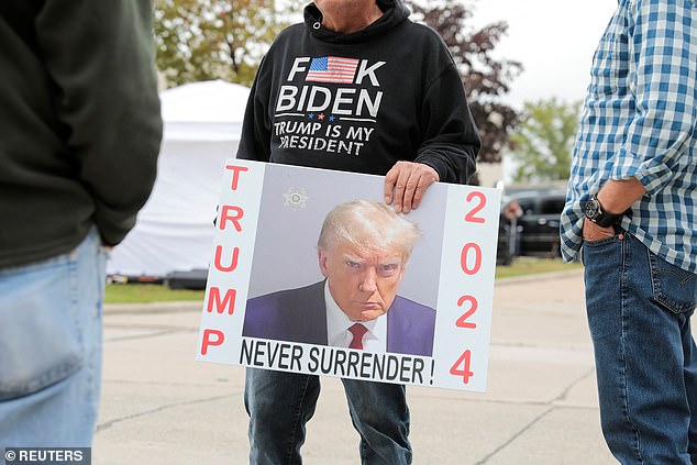 A person holds a sign with Donald Trump's mugshot in front of his rally site